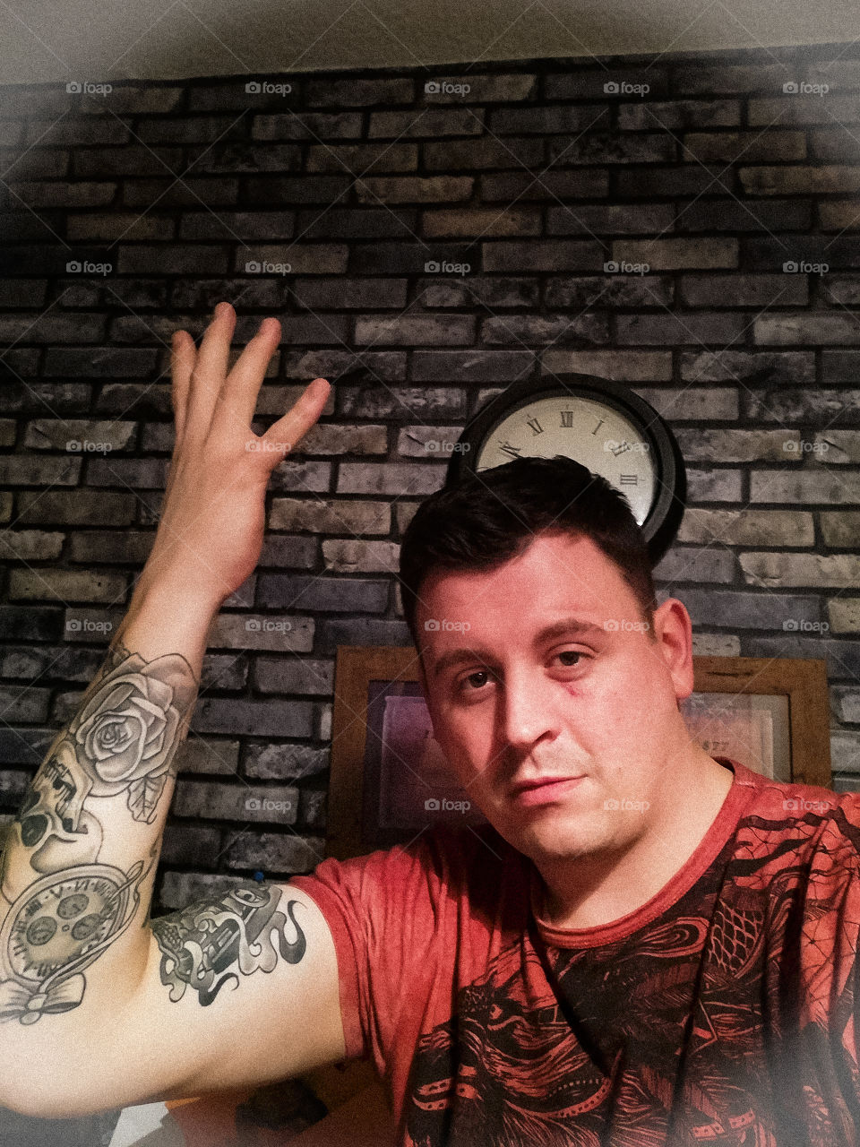 I've taken a photo of myself standing in front of a wall with a clock behind me showing off some of my tattoos I have acquired over the last couple of years