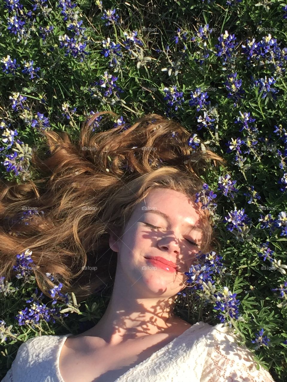 A sweet girl blissfully lays in a field of bluebonnets with her hair sprawled out around her head. 