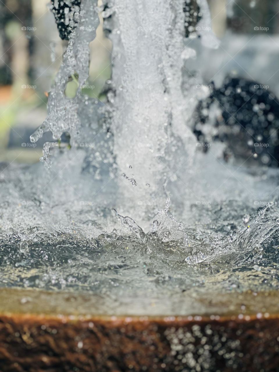 Closeup of bubbling water in a fountain in a city park. Full frame view of splashing and granite edge of fountain