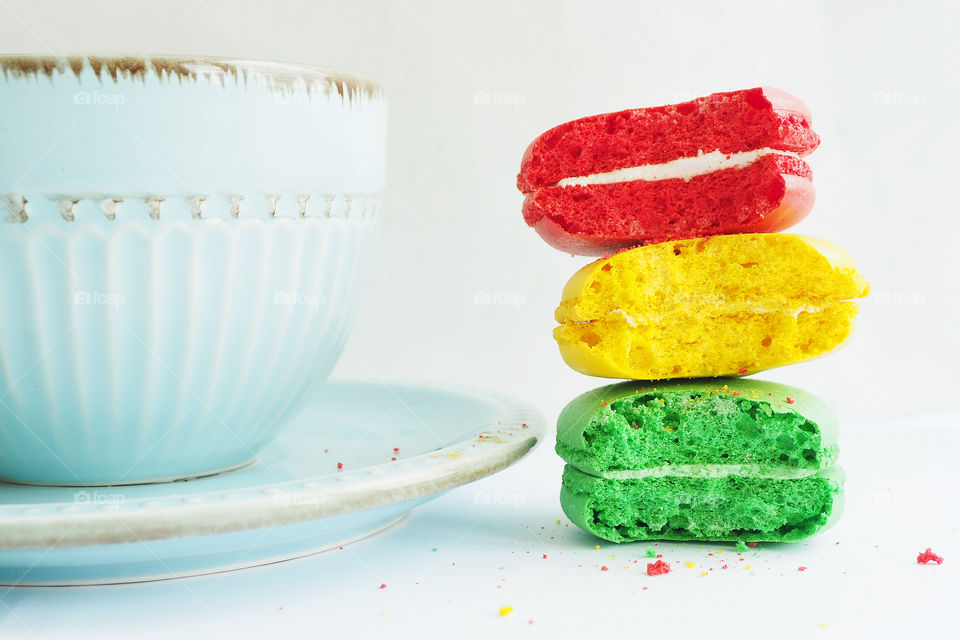 three bitten macaroons in bright colors red yellow and green next to a blue Cup on a white table