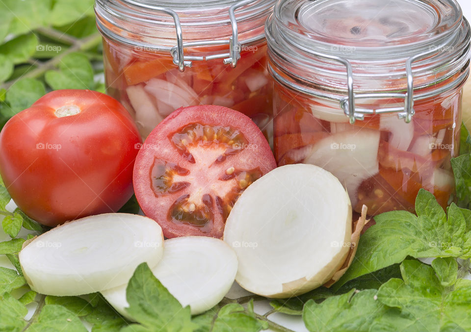 Closeup view of  tomato half and onion in front of two jars of pickled tomatoes and onions .