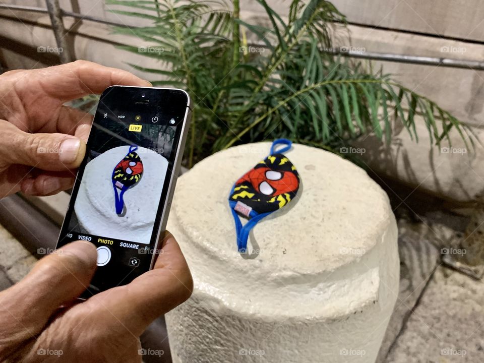 Spider man mask with red, blue and yellow color. A hand of a man holding his iphone taking picture.