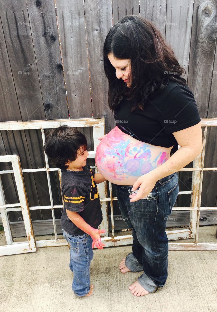 Little boy applying paint on pregnant mother's tummy