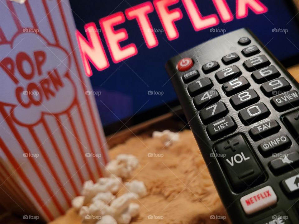 Aiming the remote control at television screen to choose favorite netflix channel to binge watch TV shows or movies for a fun and cozy night in with a popcorn snack