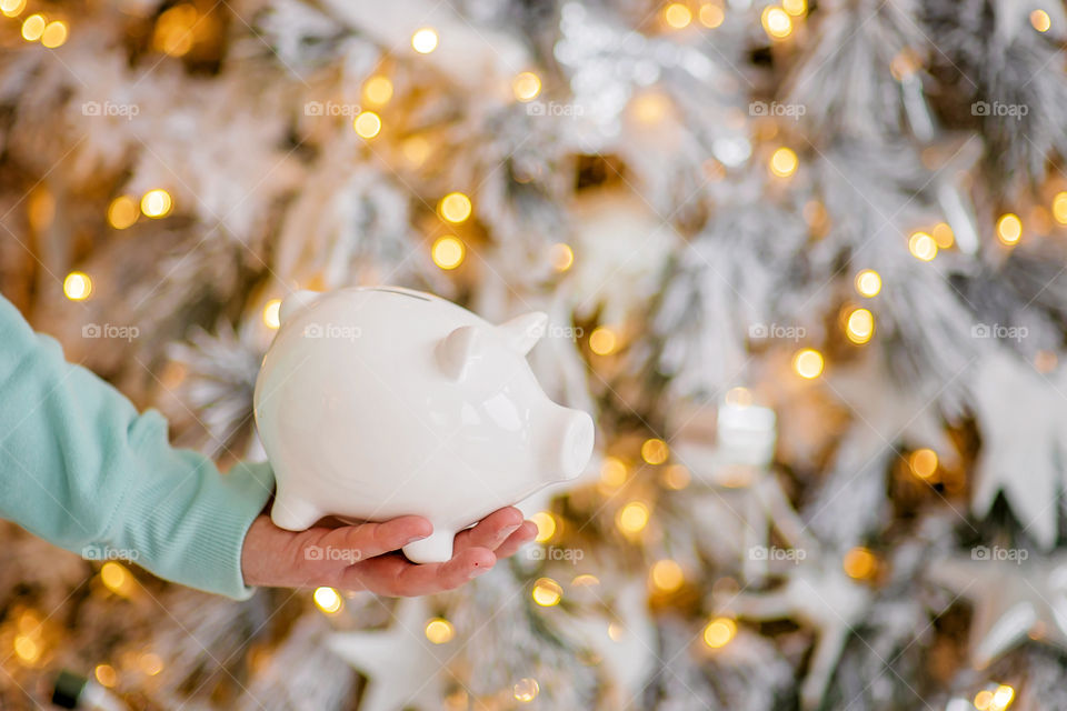 piggy bank with 100 dollars banknote in festive New Year atmosphere of scenery.  Magical bokeh with Christmas tree and bright lights.