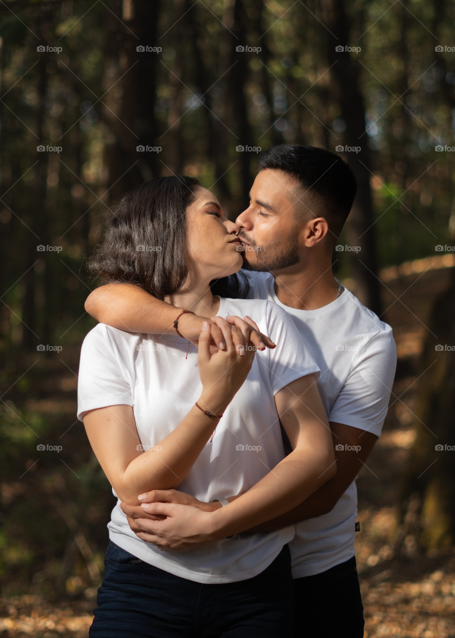 Couples of young people sitting and kissing in middle of the forest while looking into their eyes, in a sunny day.