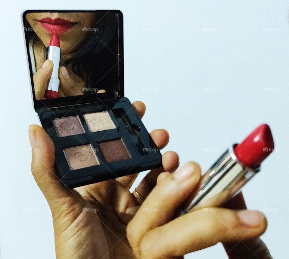 woman applying lipstick looking at a small square sized hand mirror