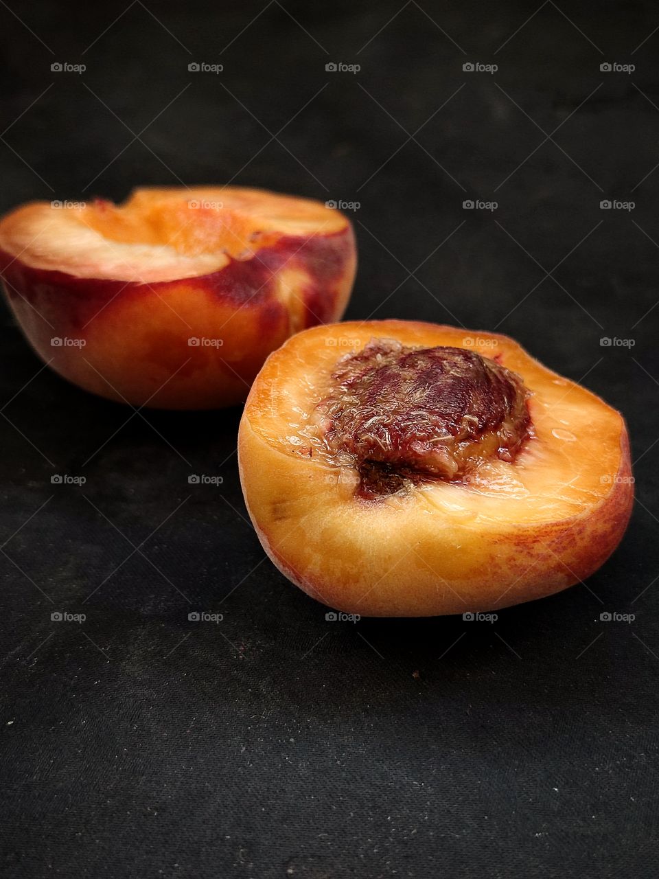 two halves of a peach on a black background.  side view