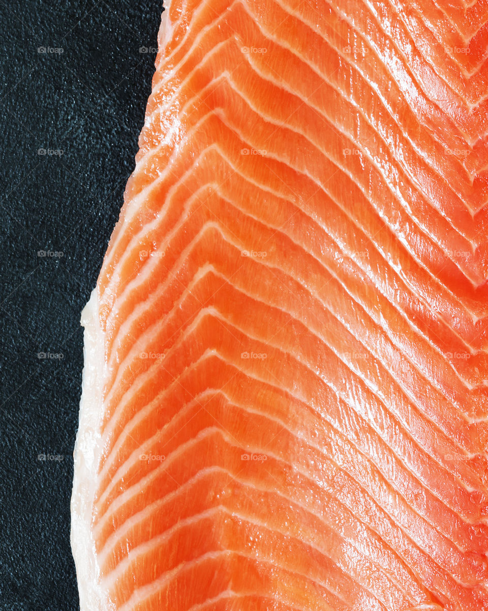 Fresh sea fish, raw salmon fillet on a black stone background with copy space. Large piece of red fish before cooking. Healthy oriental food. Top view