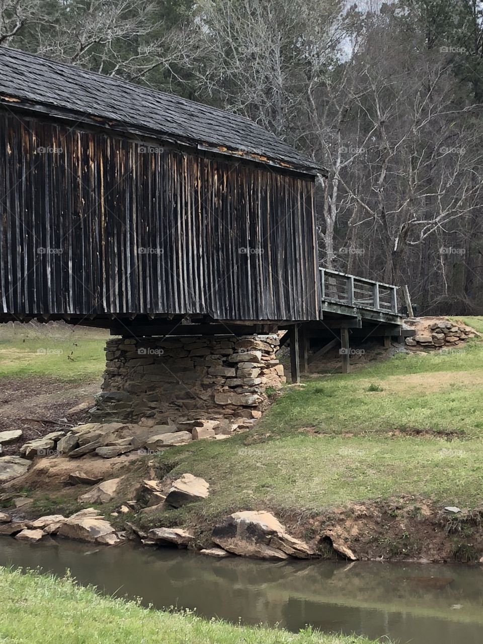 An old wooden  covered bridge from the 1800’S showing water grass, rocks. 