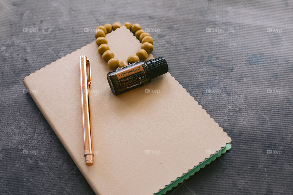 Frankincense doterra essential oil bottle on cream notebook with mustard bead bracelet and rose gold pen