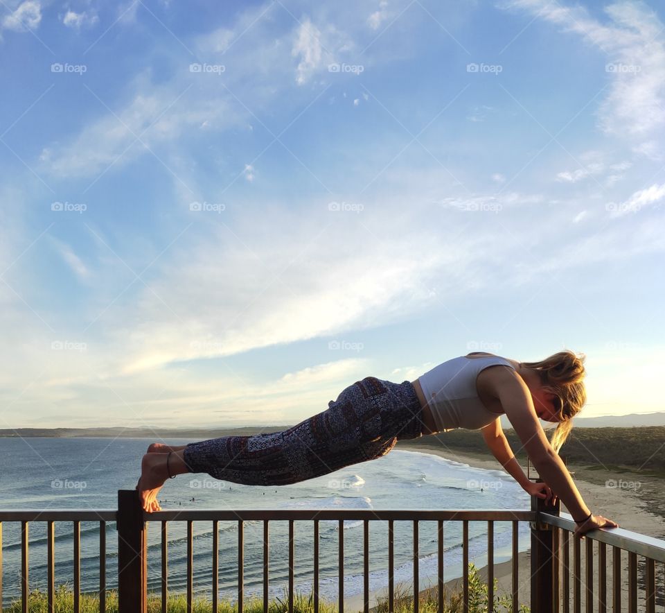 Girl holding a plank while doing sunset yoga overlooking a gorgeous Australian beach.