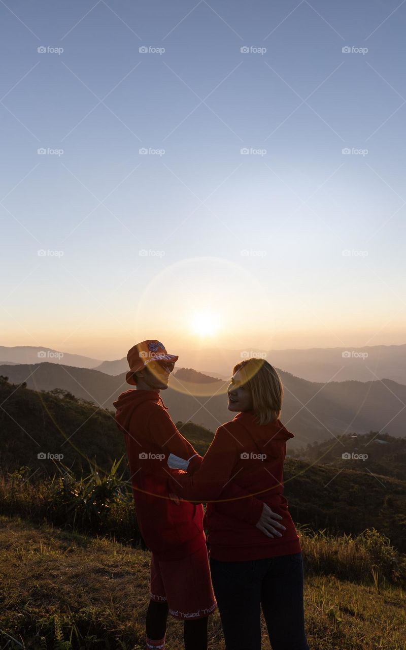 A couple with Sunset in between on Pha Tung Hill Chiangrai Thailand