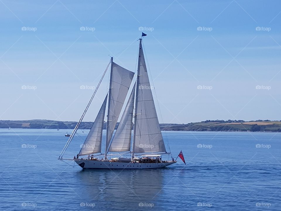 yacht sailing a calm sea on a beautiful sunny day with a coastal background
