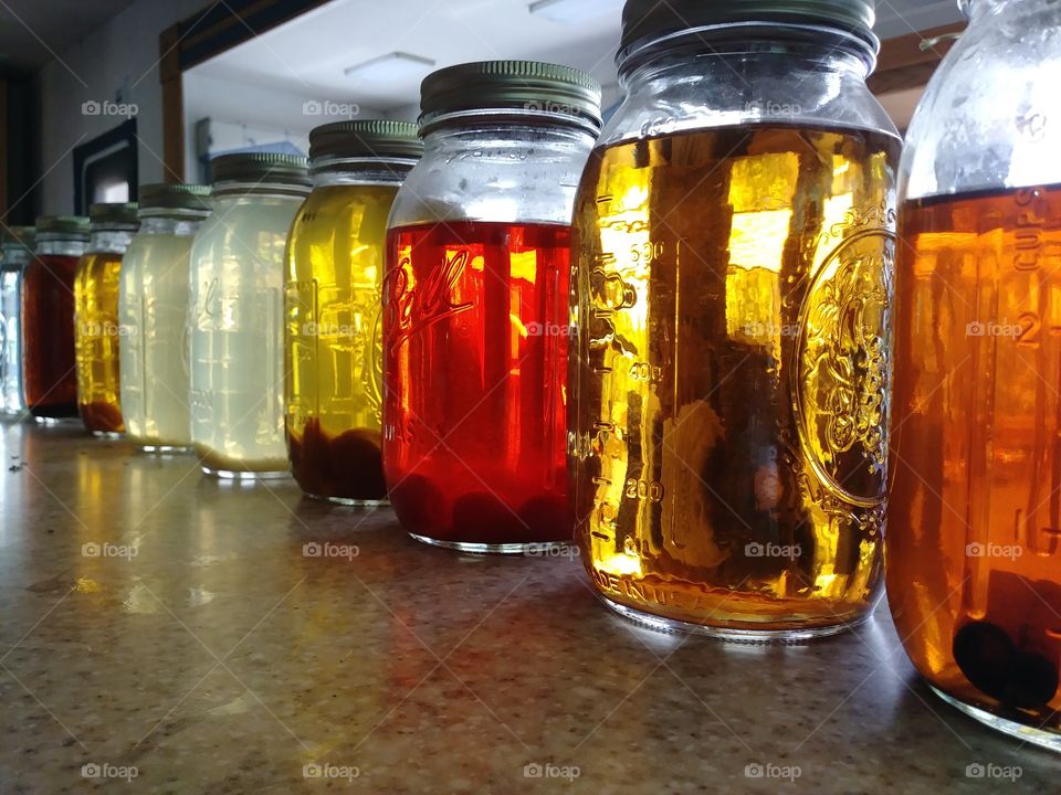 Moonshine in glass mason jars with several flavors and color varieties lined up on marble countertop