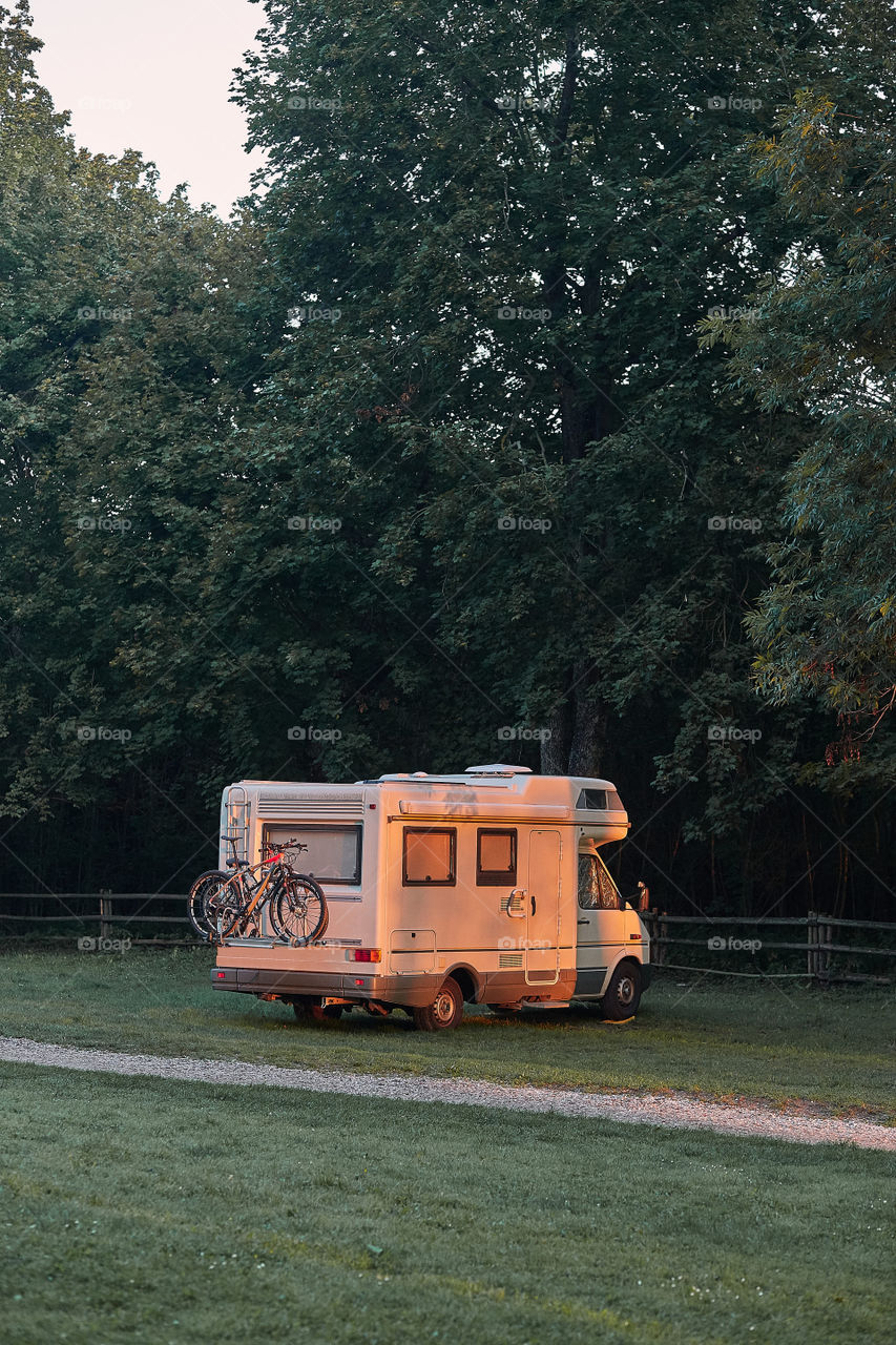 Camper van parked on camping in forest at sunrise during vacation journey. Candid people, real moments, authentic situations