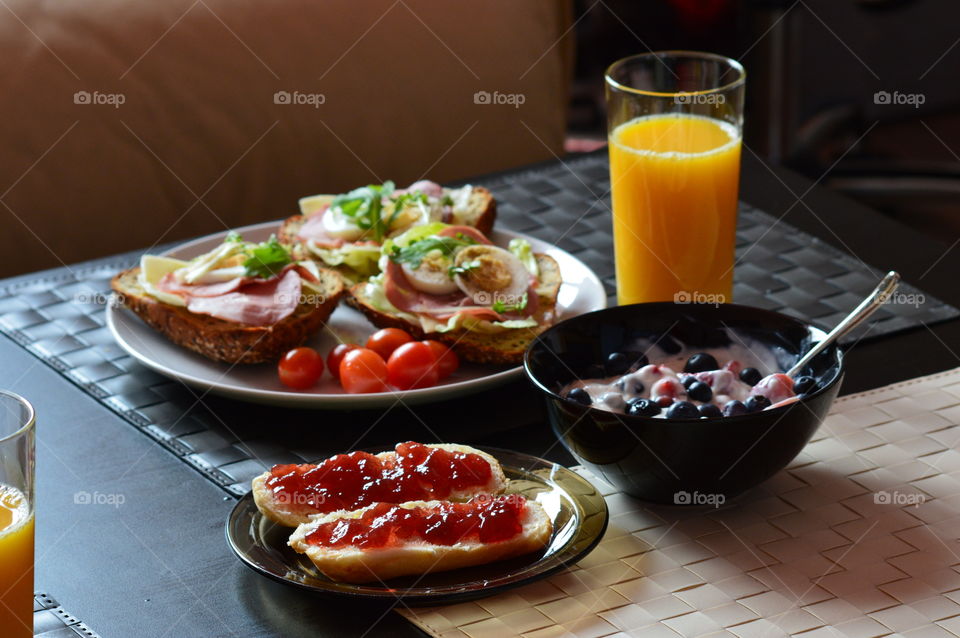 healthy breakfast full of vitamins - sandwitches of wholemeal bread with fresh lettuce, cheese, ham, egg, cress and cherry tomatoes plus yogurt with fresh fruit strawberries and blueberries and scones with jam plus freshly squeezed orange juice