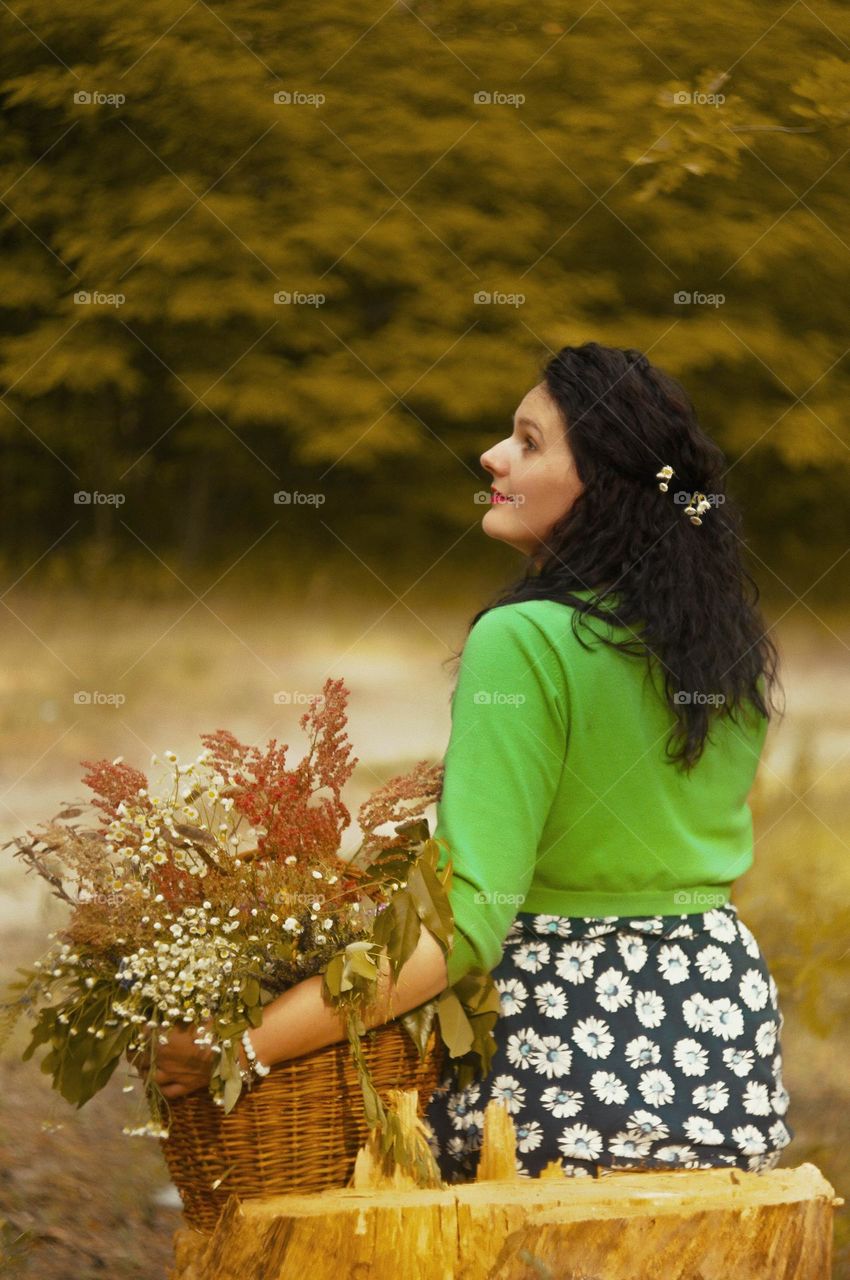 portrait of a mother in a green forest with a basket of flowers