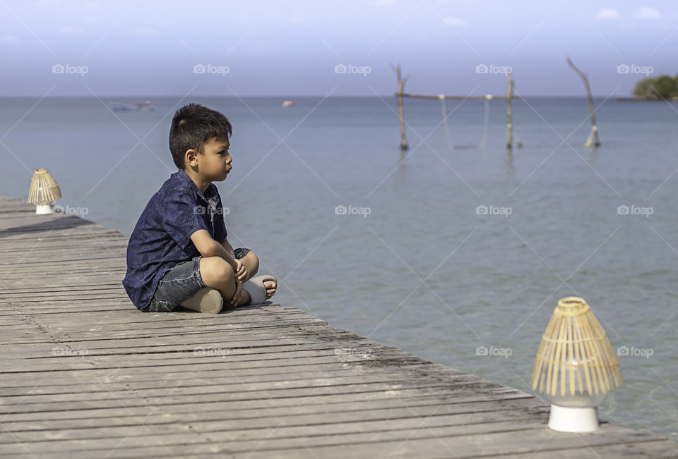 Asian boy on the wooden bridge pier boat in the sea and the bright sky at Koh Kood, Trat in Thailand.