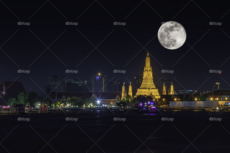 Wat Arun at night with Light gold is the oldest temple of the Chao Phraya River and Full moon In the dark sky in Bangkok Thailand.