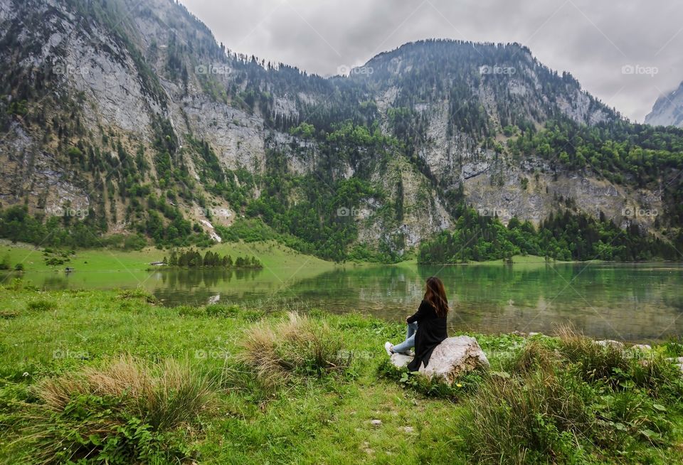 Back of people from behing, female person sitting on rock and enjoying peaceful scenic of lake and mountains in Germany in springtime 