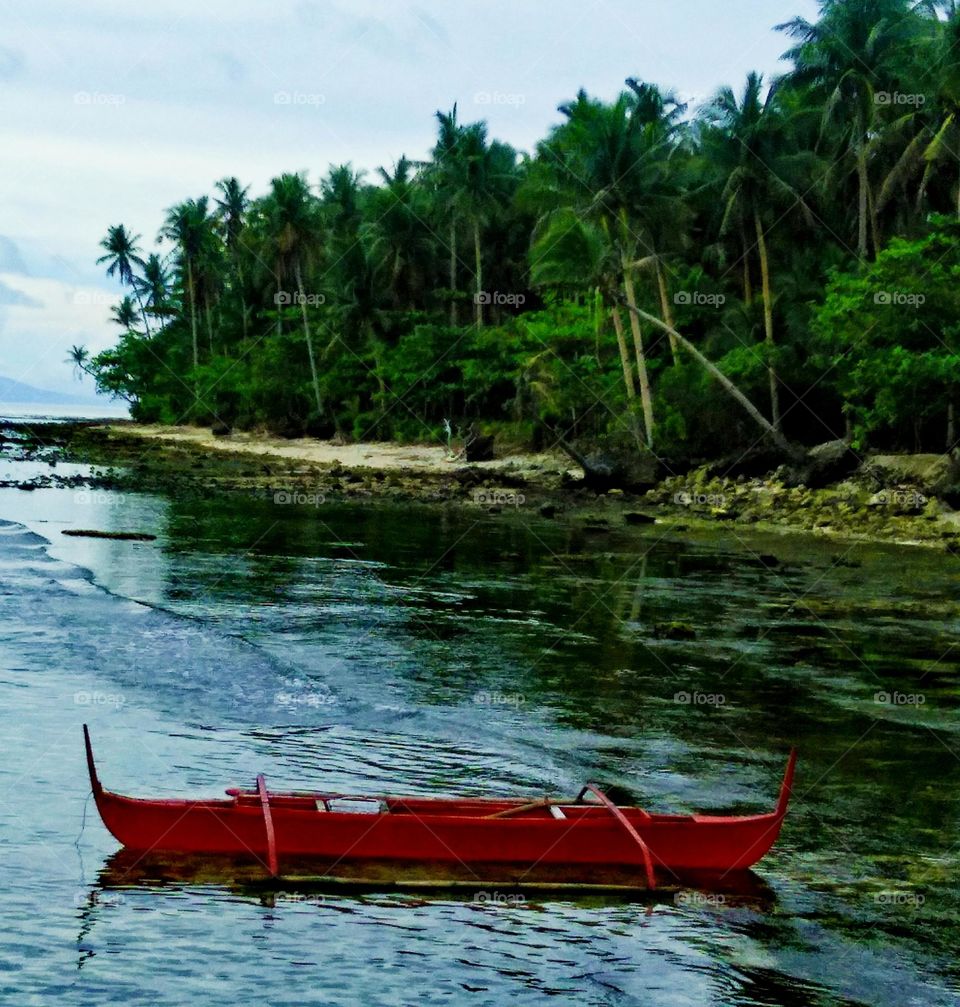 Traditional Indigenous Filipino wooden outrigger banca boat anchor at tropical island surrounded with calm, crystal clear body of seawater.