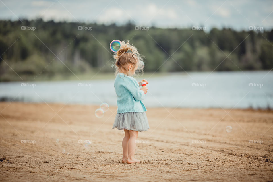 Little girl on lake coast at sunny evening. 