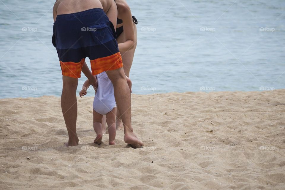 Toddler hold by his parents on the ground of the beach 