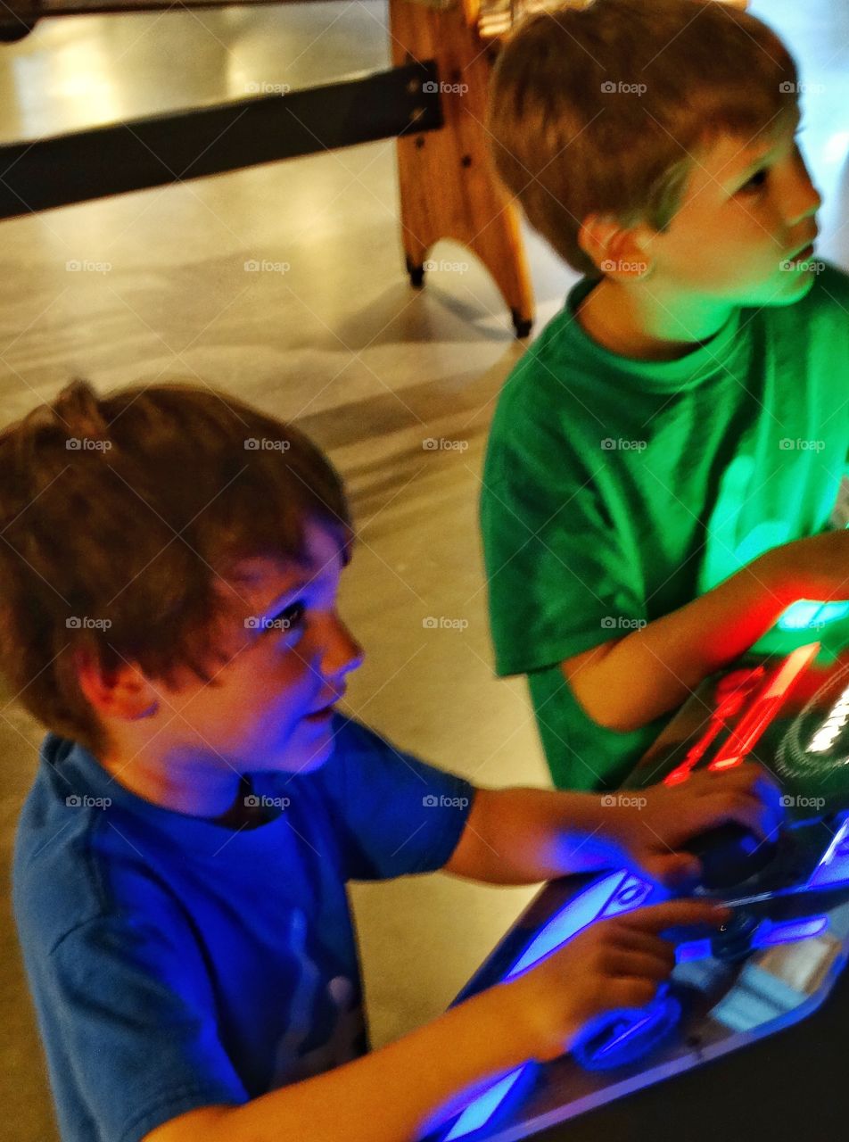 Boys Playing A Videogame. Young Brothers Lit Up By A Colorful Electronic Control Panel
