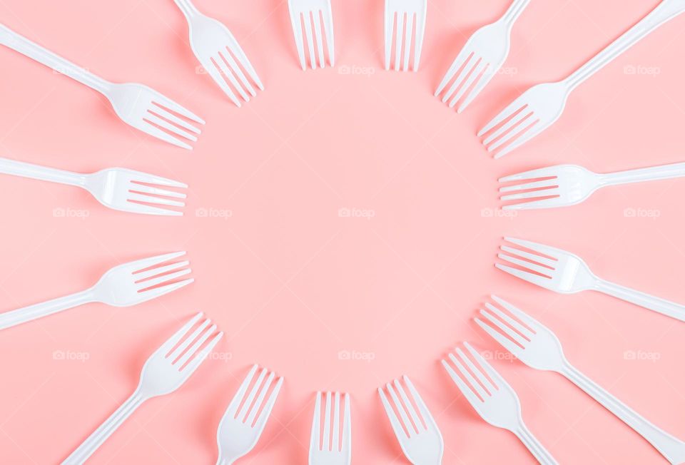 Lots of white plastic vids lying in a round frame with copy space in the center on a pink background, flat lay close-up. Cutlery and ecology concept.