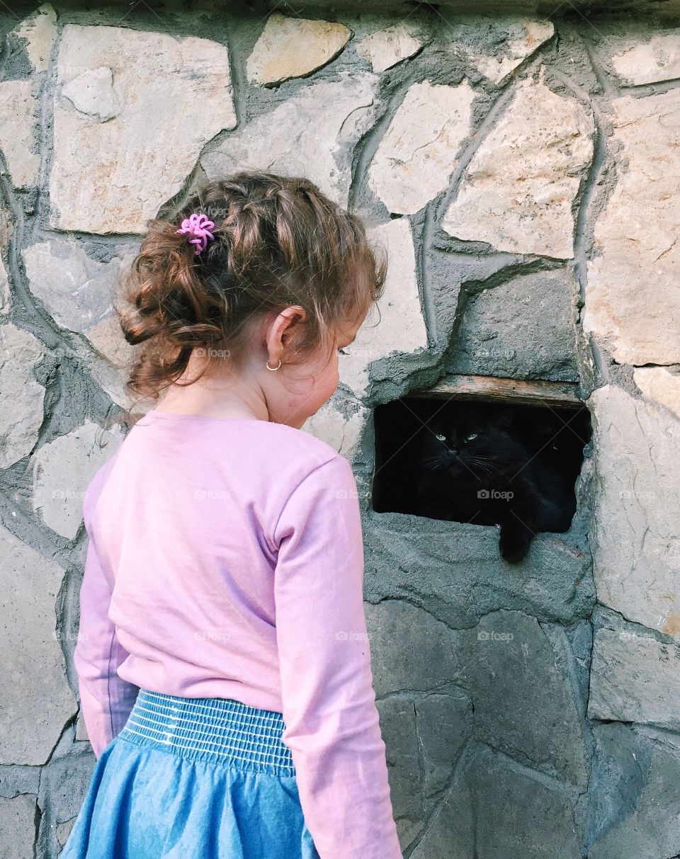 Cute girl meeting black cat in little window. 