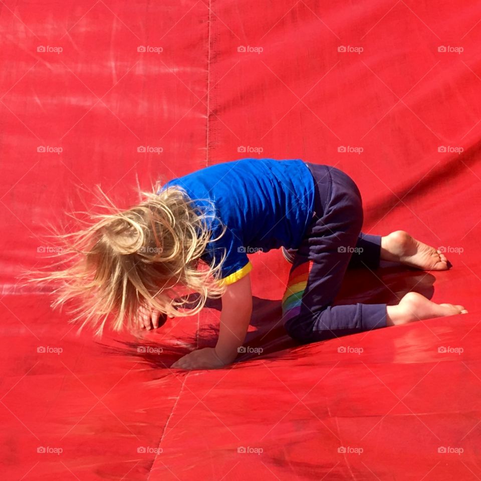 Young boy tumbling down a red inflatable slide in north devon - Spring sunshine lights the photo 