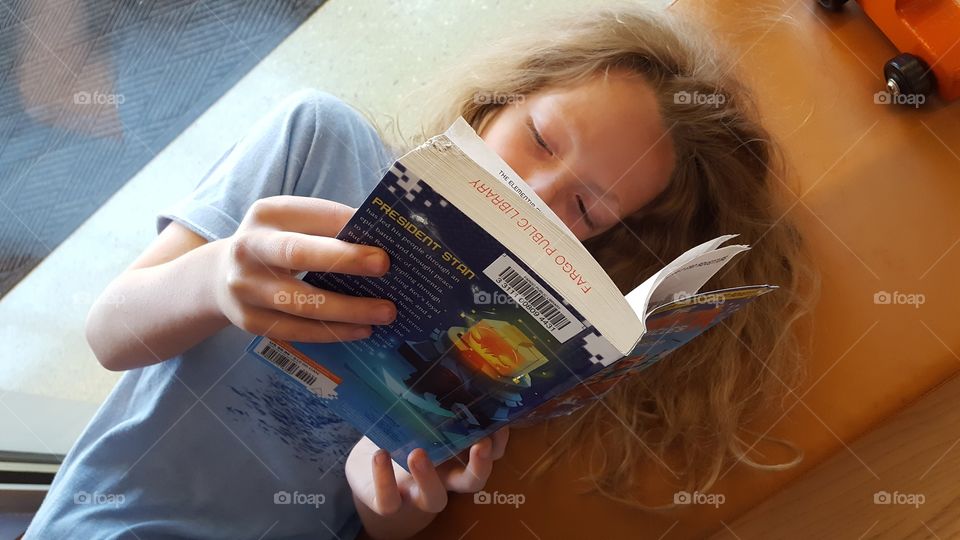 child reading a book stamped with Fargo Public Library.