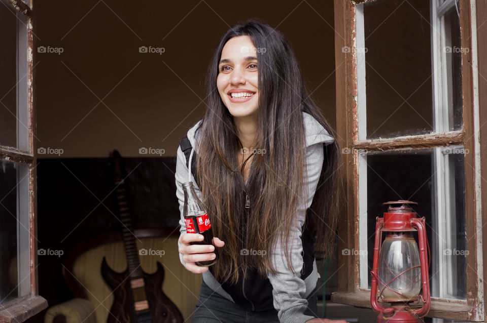 Beautiful woman holds Coca-Cola bottle on the window and smiling