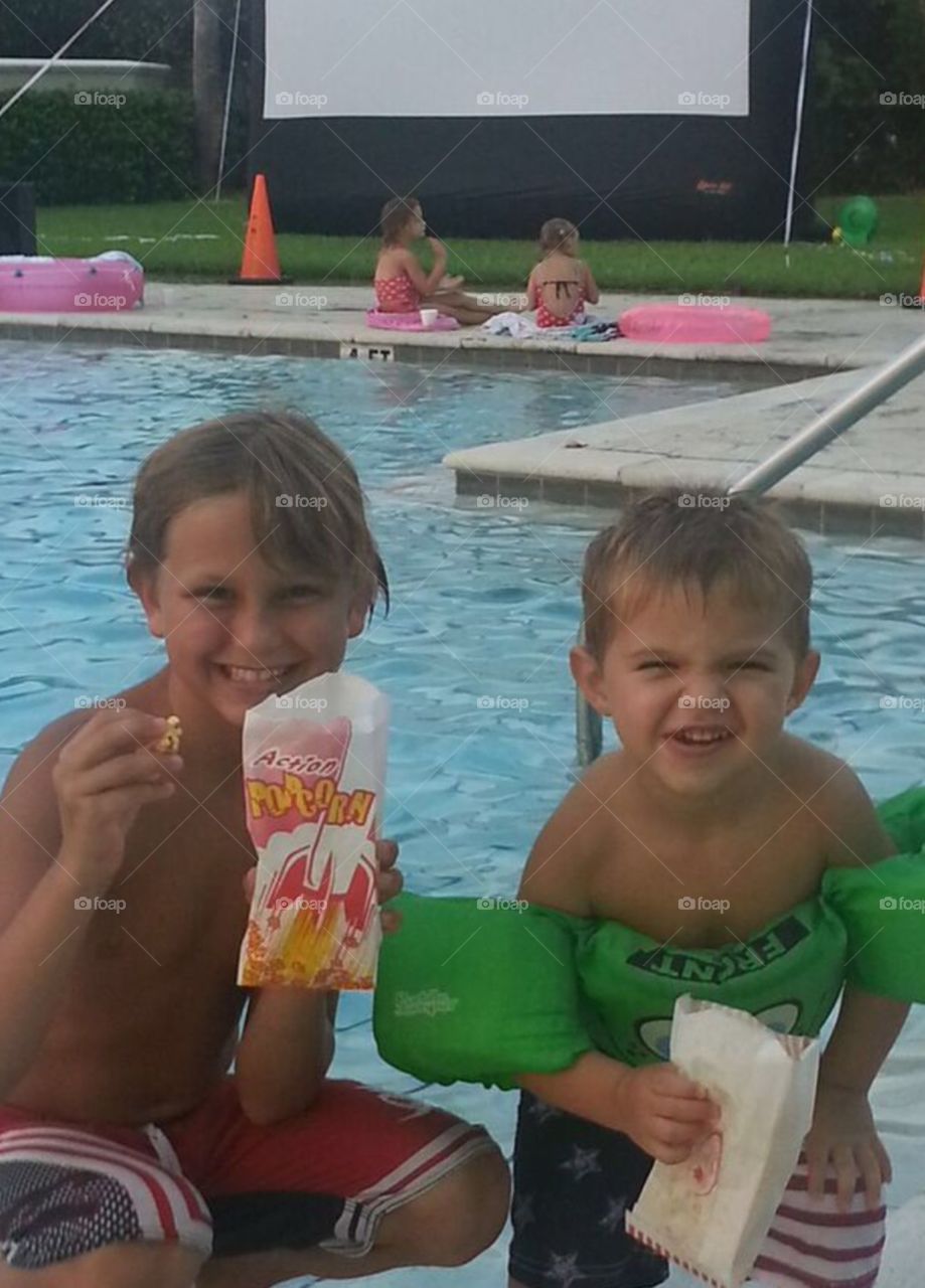 Movie by the pool. . 2 boys eating popcorn waiting for the movie by the pool to start. 