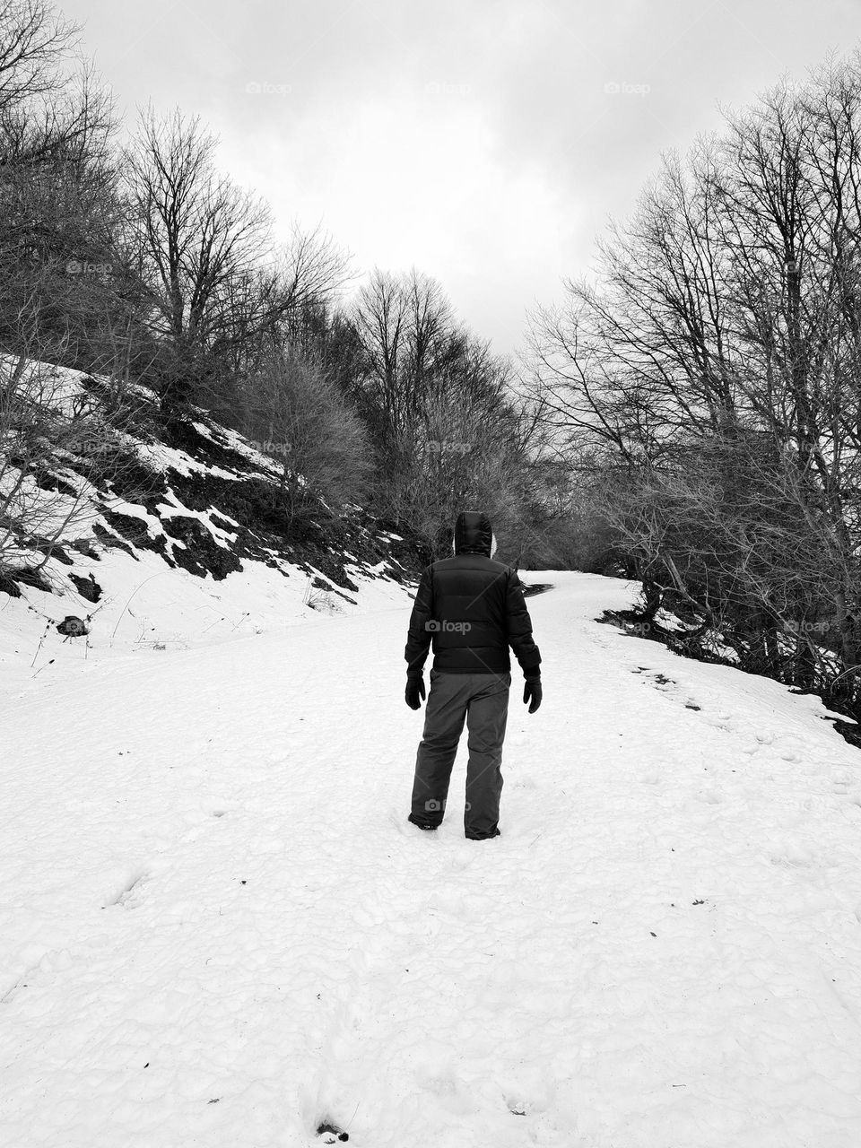 man from behind hooded for the cold walks on the snow in the mountains