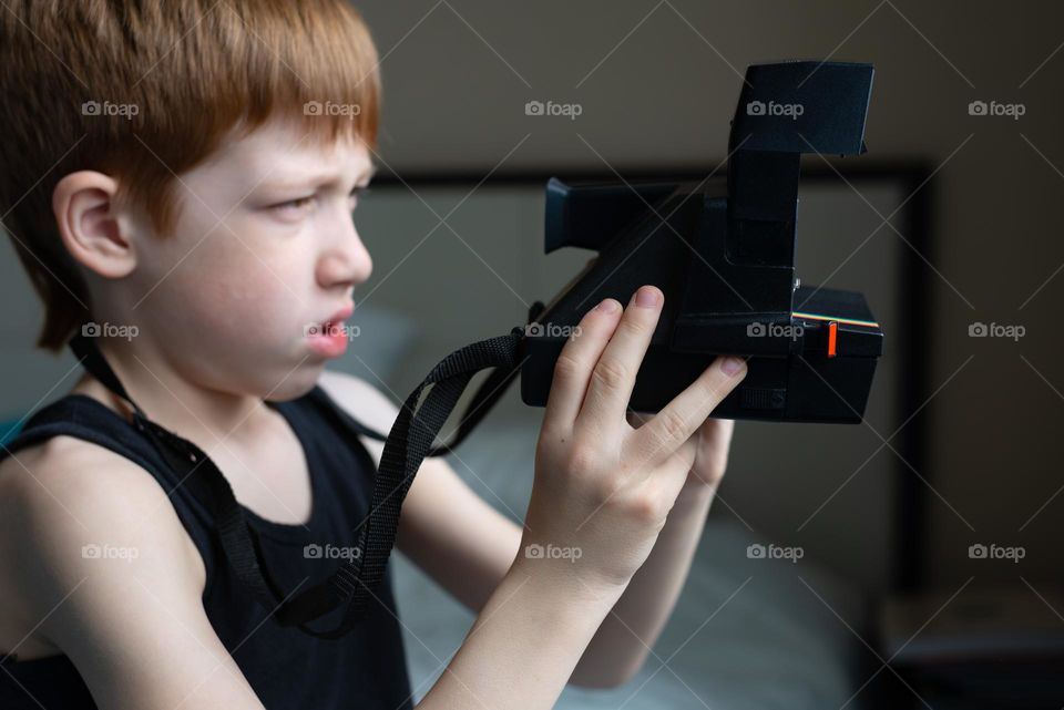 Child red-haired boy with a palaroid camera in his hands, filming life