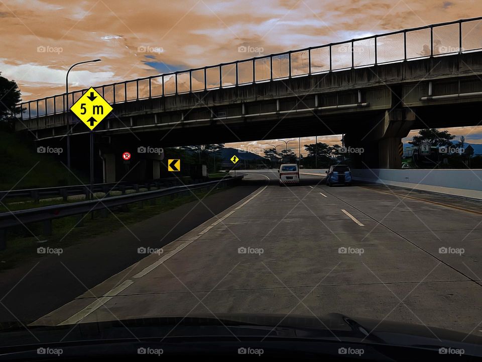 Driving on toll road, traffic sign, flyover space height, warning signs, 5 meter traffic sign, the toll road view is very beautiful, a cllection of brown an bright clouds, yellow brown sky, beauftiful natural outdoor scenery