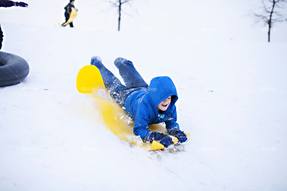 Boy sledding down a hill face first in the winter 