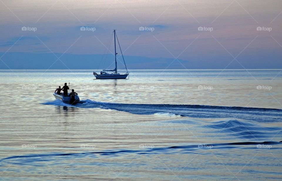 People travelling in motorboat leaving water trails