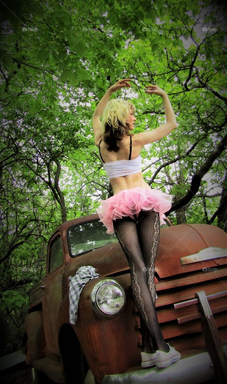 Thin, long-legged All-American girl poses in a tutu on the front bumper of a classic truck.