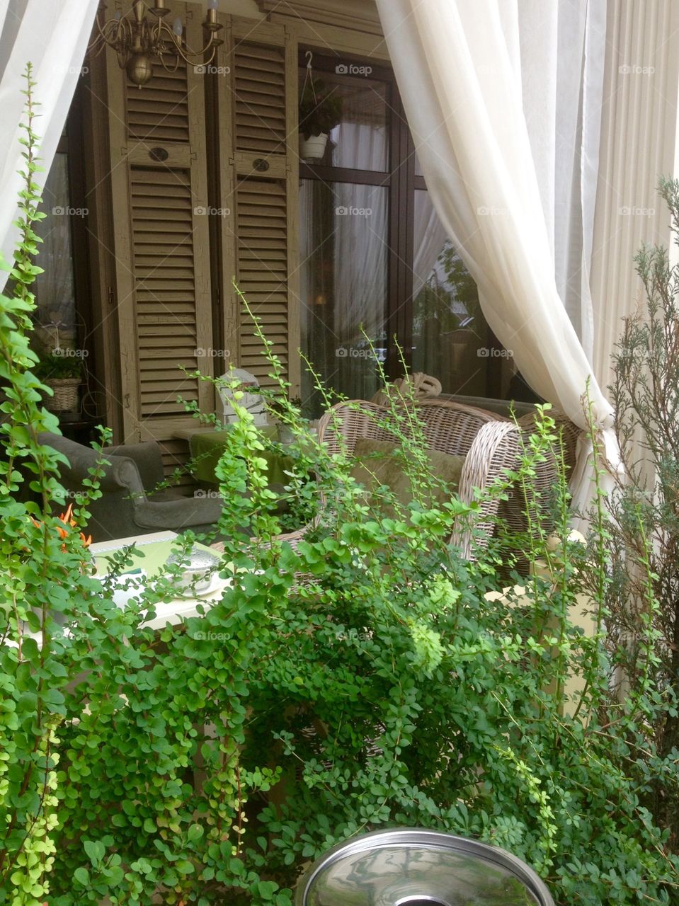 Terrace with cane furniture from the yard with bushes