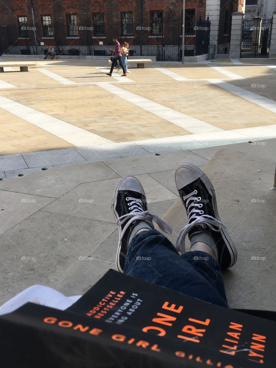 A picture of a persons legs crossed with the book Gone Girl on their lap. Taken in a public square in London. 