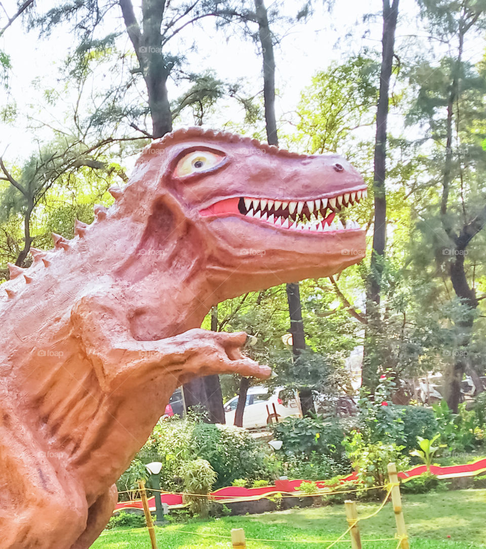 The small park in the statue of dinosaur, it's a toy, the dinosaur is smile here. it's like fun