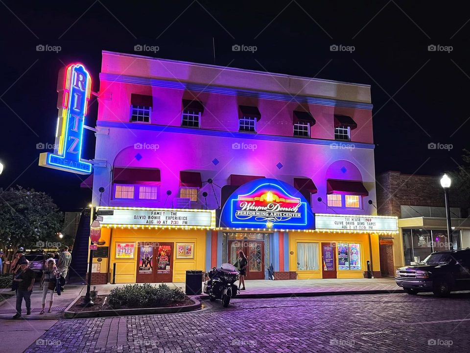 Nighttime street scene with purple and yellow theater building lit up with neon lights.