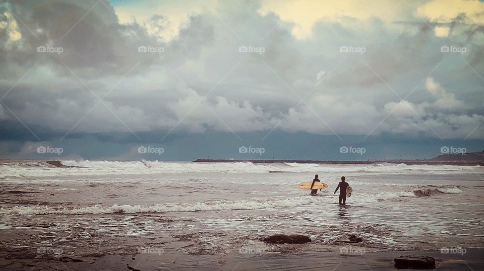 Two surfers head out into open water as a rainstorm begins to make its presence known. Ocean Beach, California 