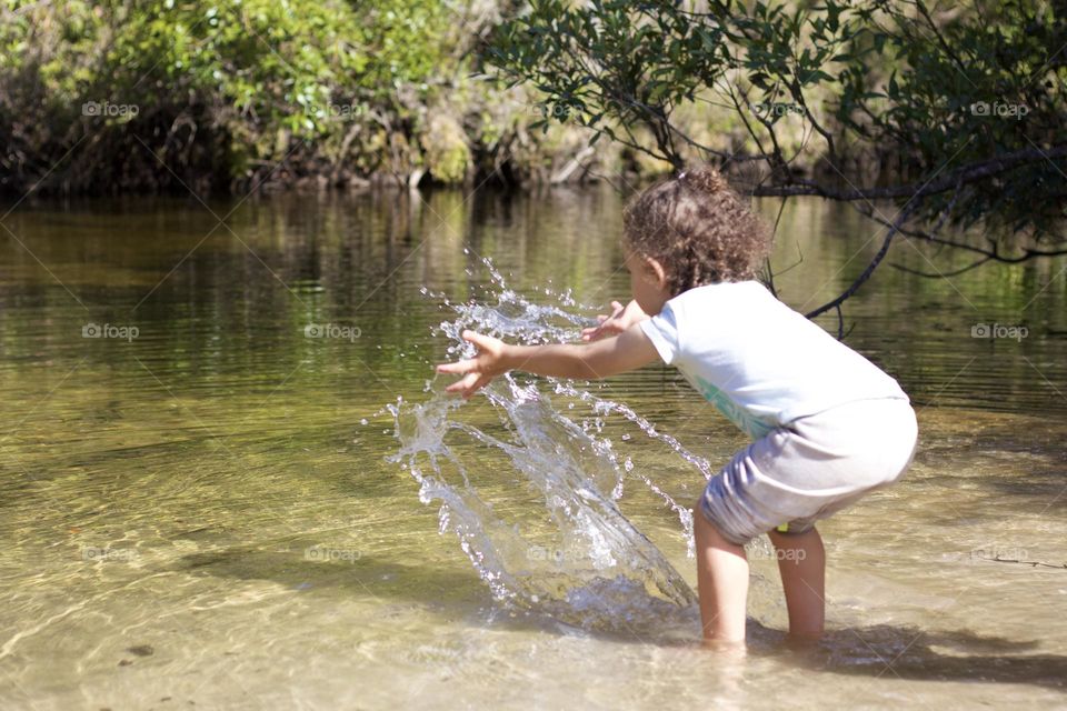 Little girl playing with river water on a hot summer day