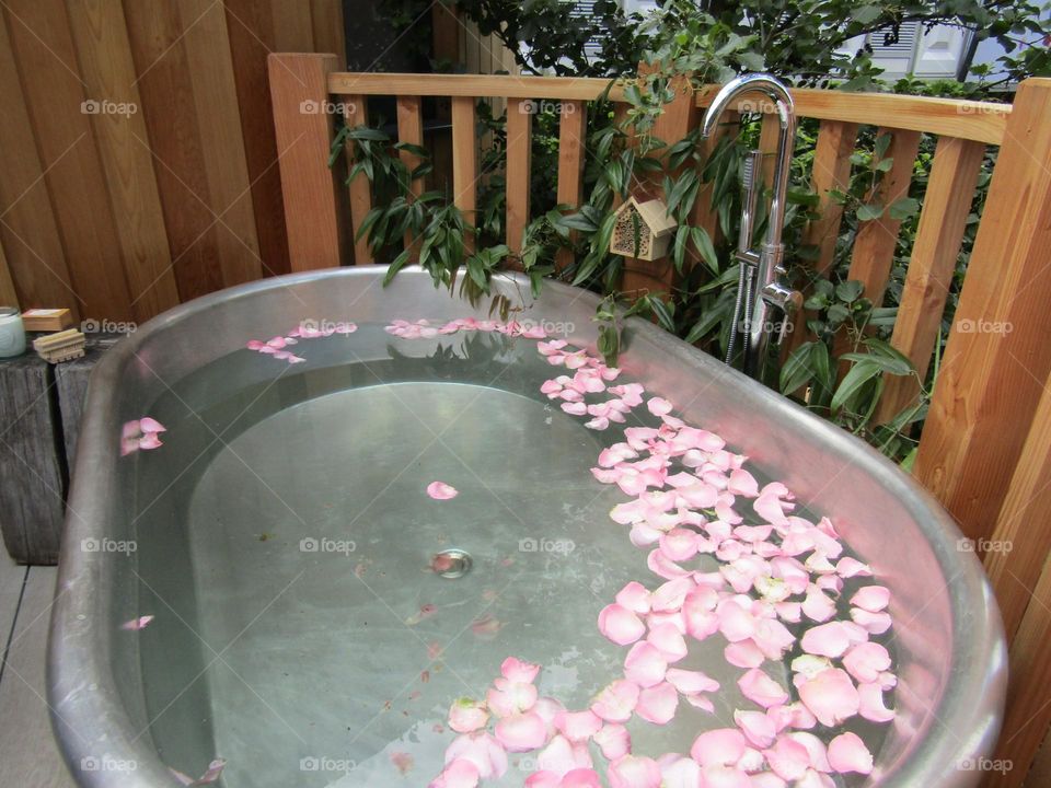 Outdoor tin bath with rose petals floating on the water. This bath is actually on a platform of a treehouse. photo taken at chelsea flower show