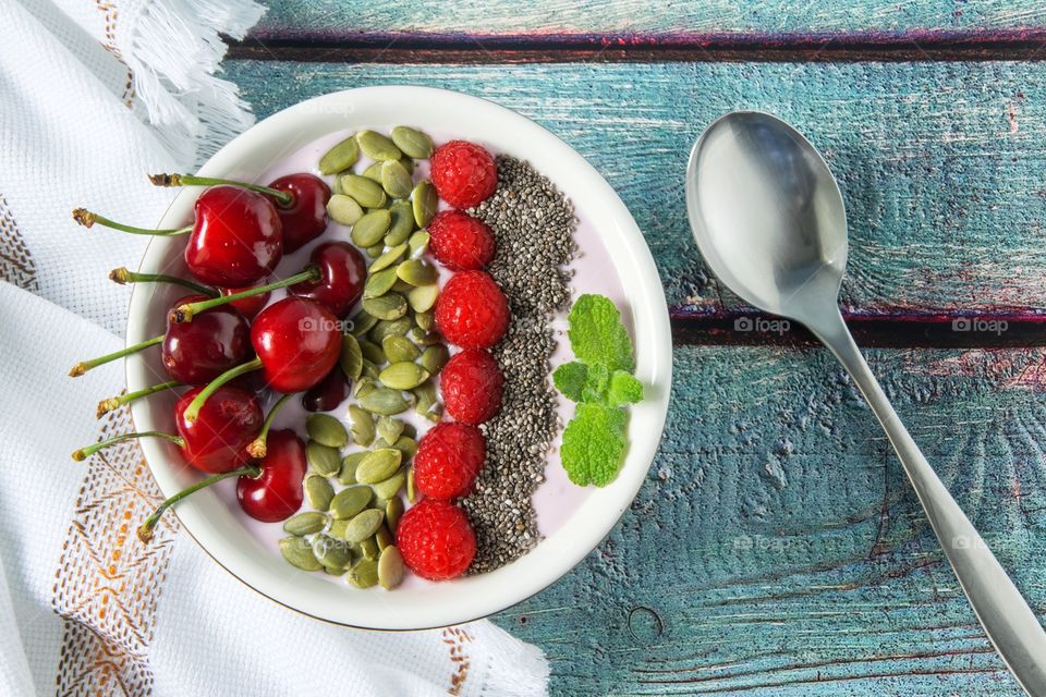 Yoghurt, banana and strawberry smoothie topped with cherries, radpberries, pumpkin seeds and chia seeds