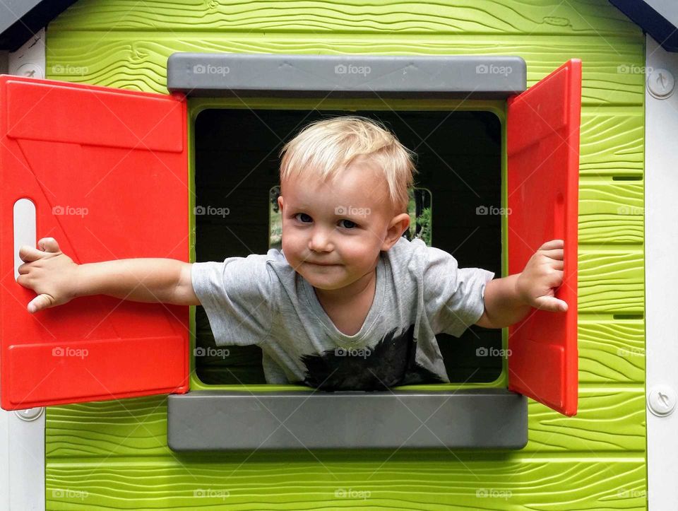 Little boy peeking out a window in a playhouse